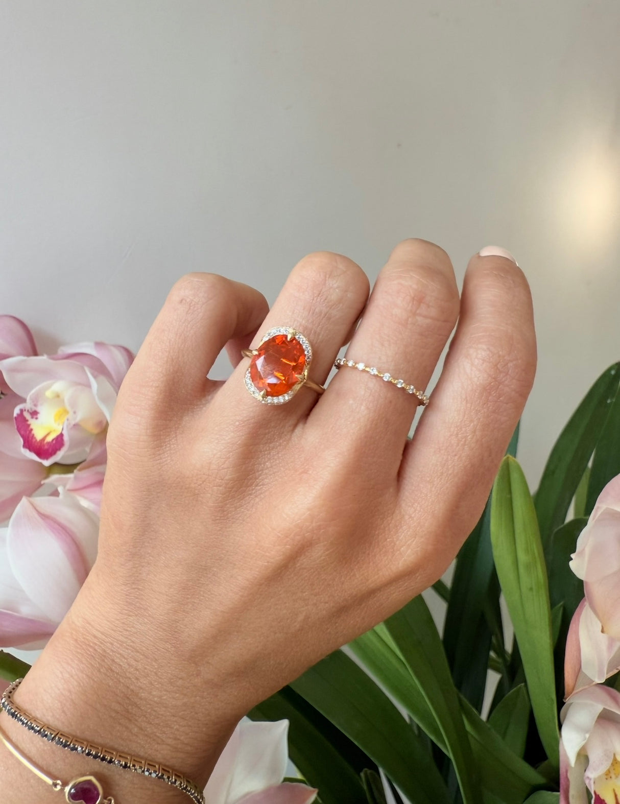 Orange fire opal gold engagement ring worn on model against a floral background.