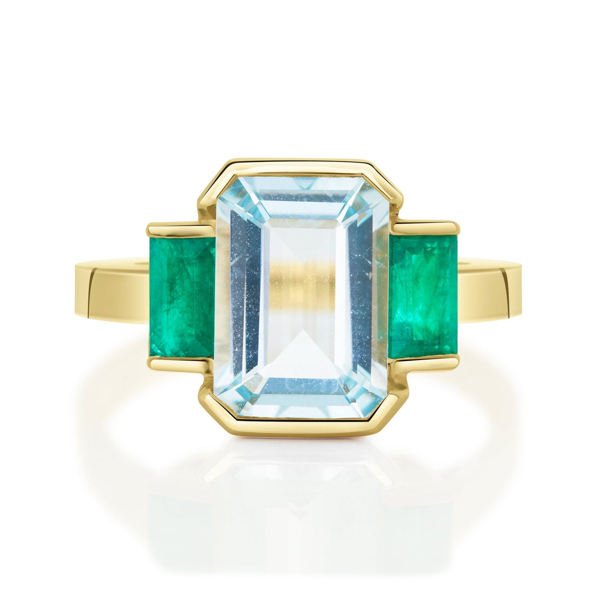 An 18K gold ring with a central aquamarine gem flanked by two vivid green emerald gems on the sides.
