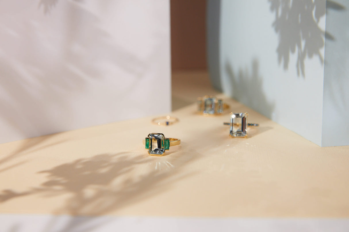An 18K gold ring with a central aquamarine gem flanked by two vivid green emerald gems on the sides. Handmade by female artisans with sustainably mined gemstones. Exquisite and modern in design.