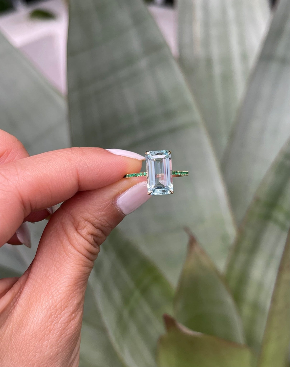 An 18K gold ring with a central aquamarine gem flanked by vivid green emerald gems on the sides. Handmade by female artisans with sustainably mined gemstones. Exquisite and modern in design. Perfect engagement ring or wedding ring.