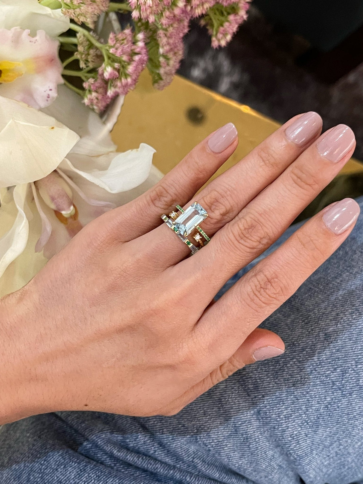 An 18K gold ring with a central aquamarine gem flanked by vivid green emerald gems on the sides. Handmade by female artisans with sustainably mined gemstones. Exquisite and modern in design. Perfect engagement ring or wedding ring.