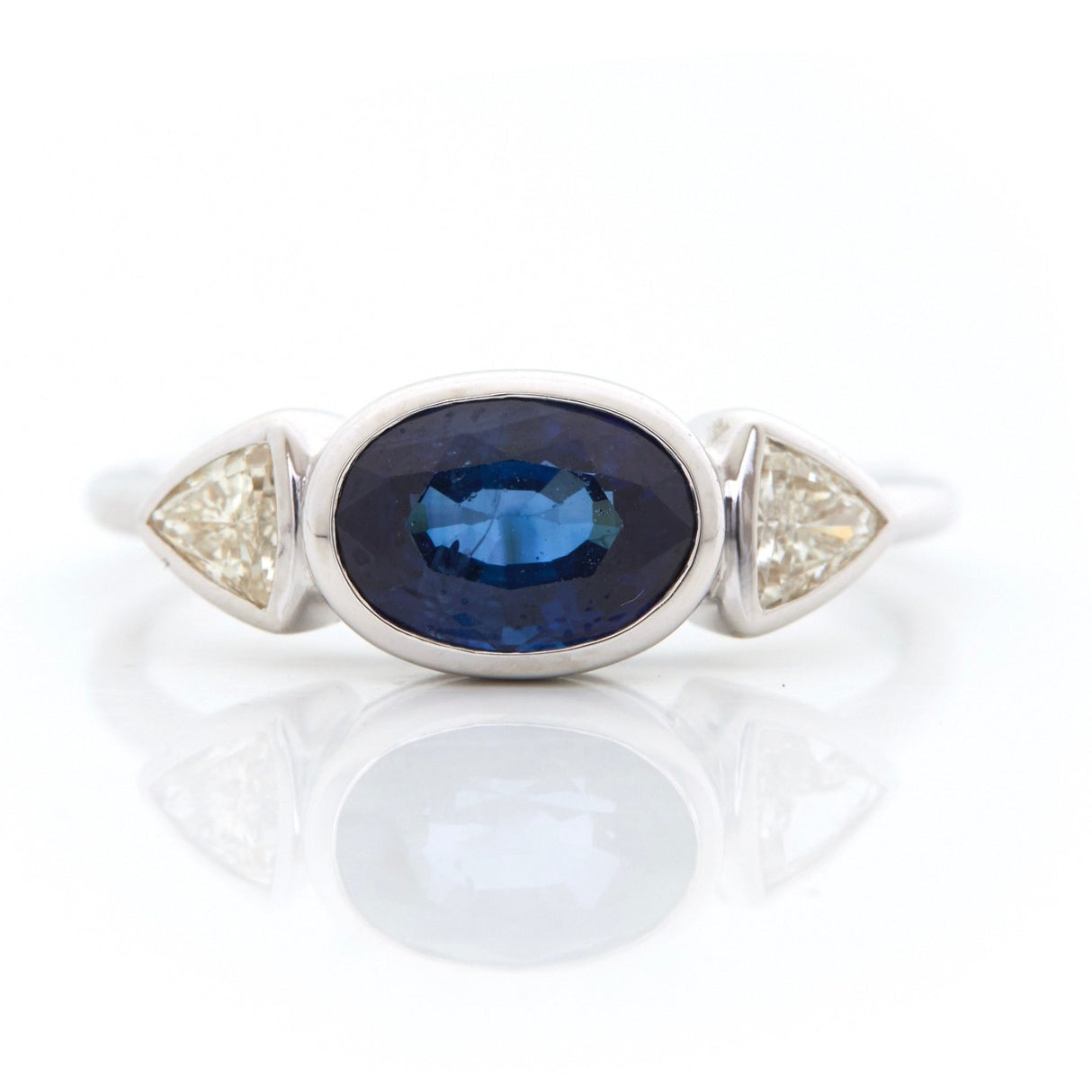 A Ceylon Sapphire and diamond ring with a large blue sapphire center stone flanked by two trillion-cut diamonds, set in an 18k white gold band.