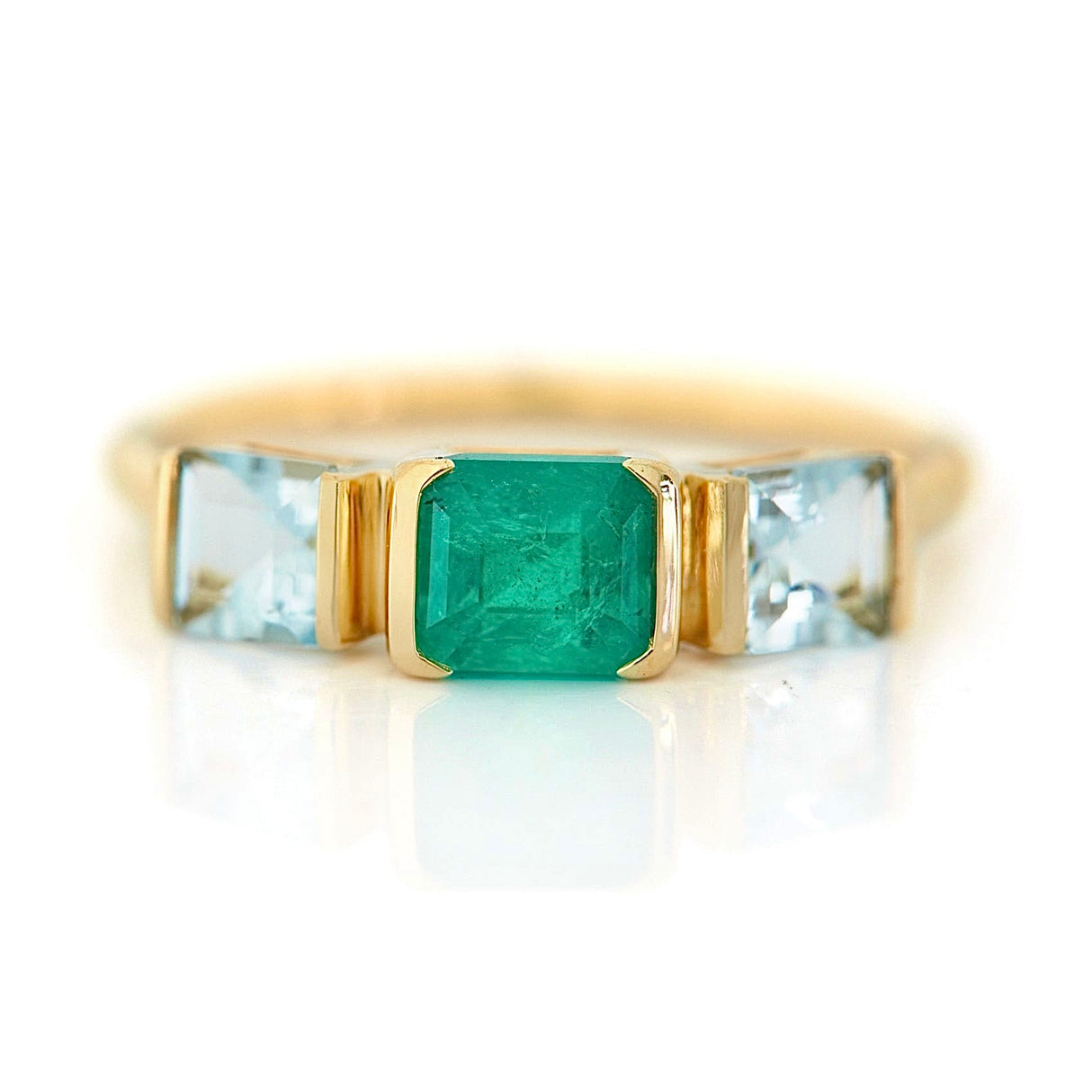A gold ring featuring a central emerald triplet flanked by two aquamarines, with a linear chic silhouette. Handmade by female artisans with sustainably mined gemstones.