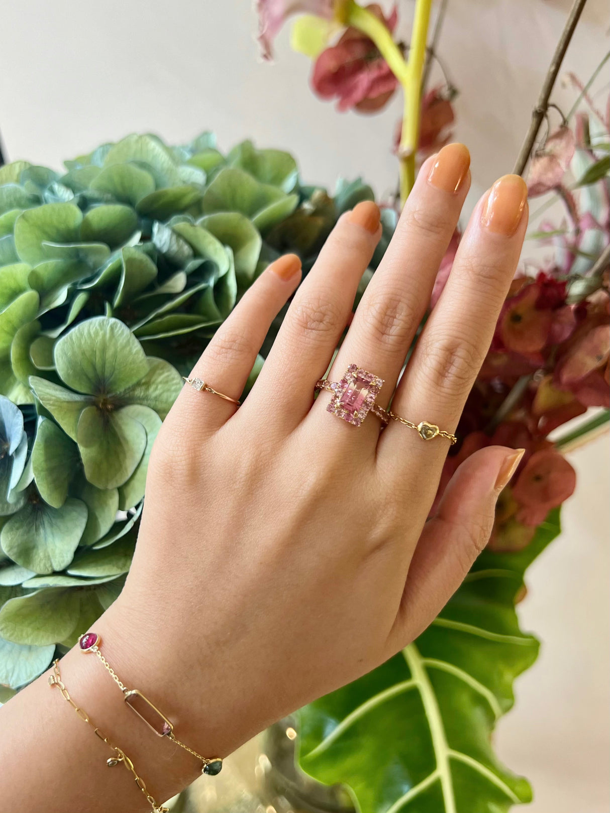 An ombré pink Tourmaline ring with a central, rectangular pink tourmaline surrounded by smaller pink tourmalines set in a gold band on model.