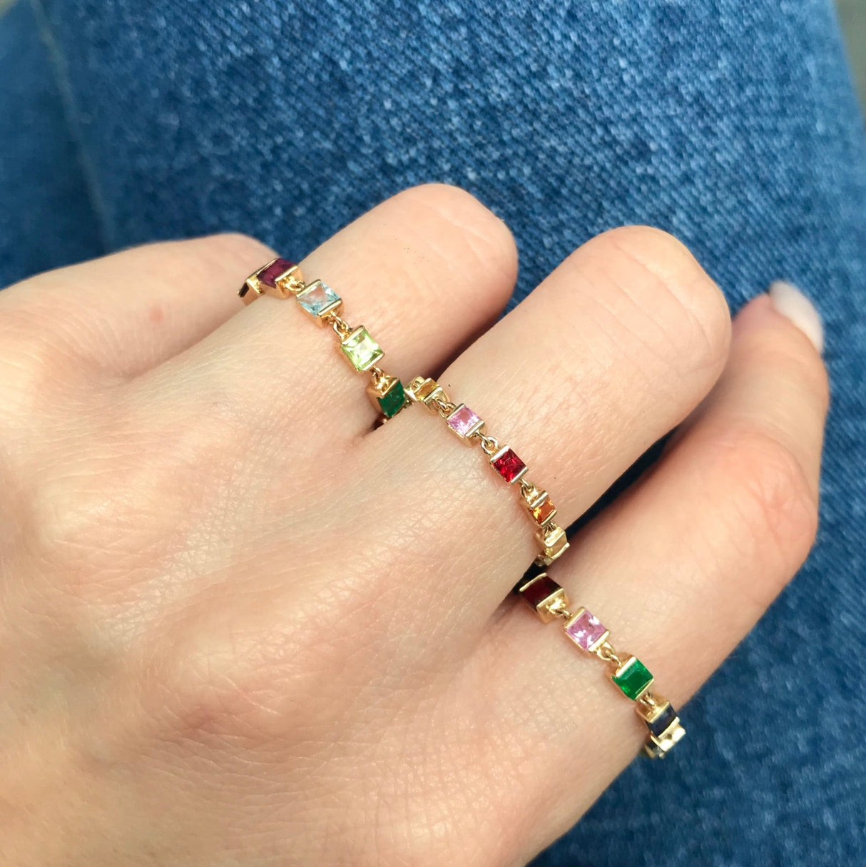 Hand wearing a colorful gemstones ring in 14k in a rain stack against a blue denim background by YI COLLECTION