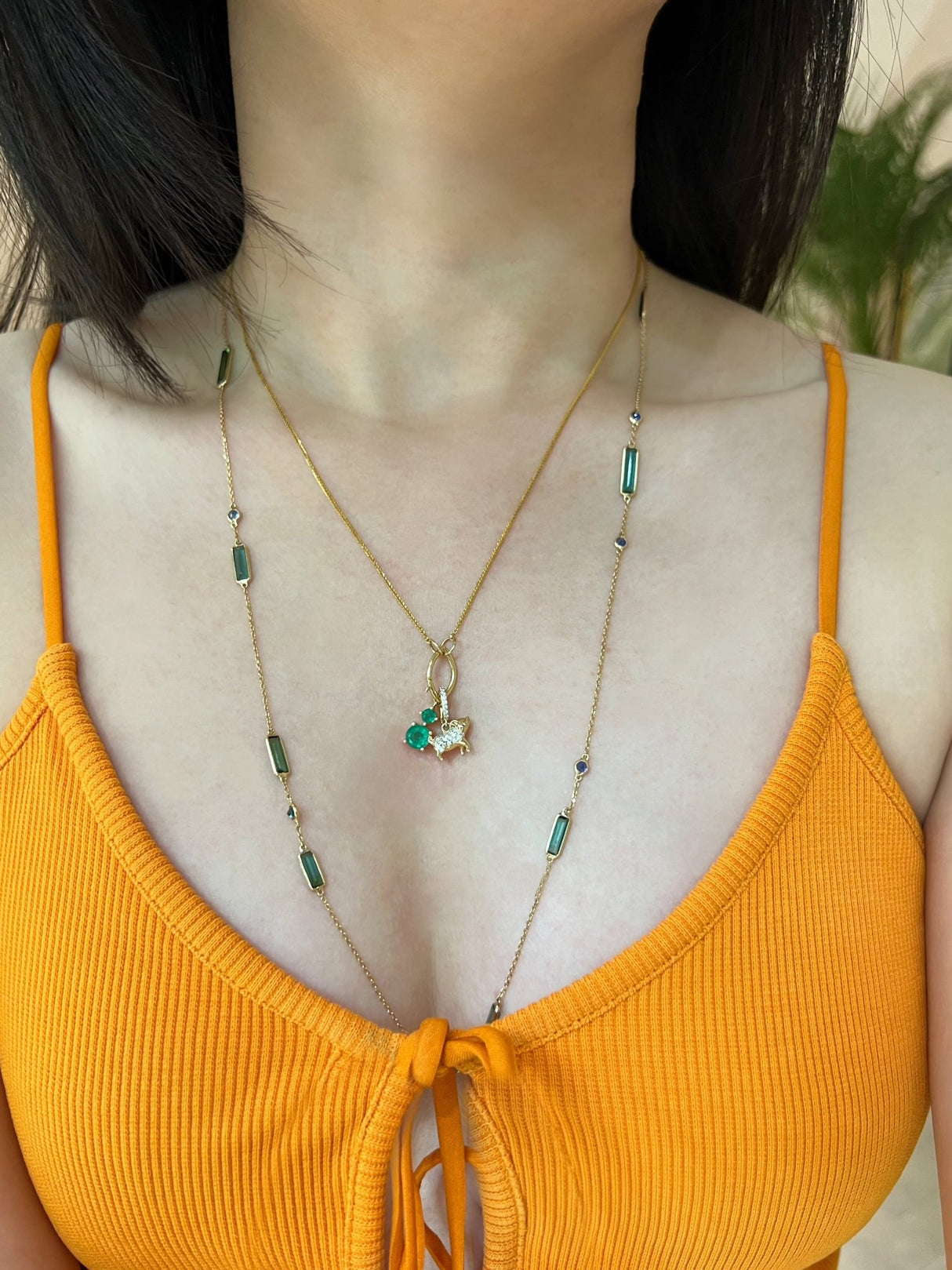 Person wearing a yellow top and gold Chinese zodiac necklace with a green pendant.