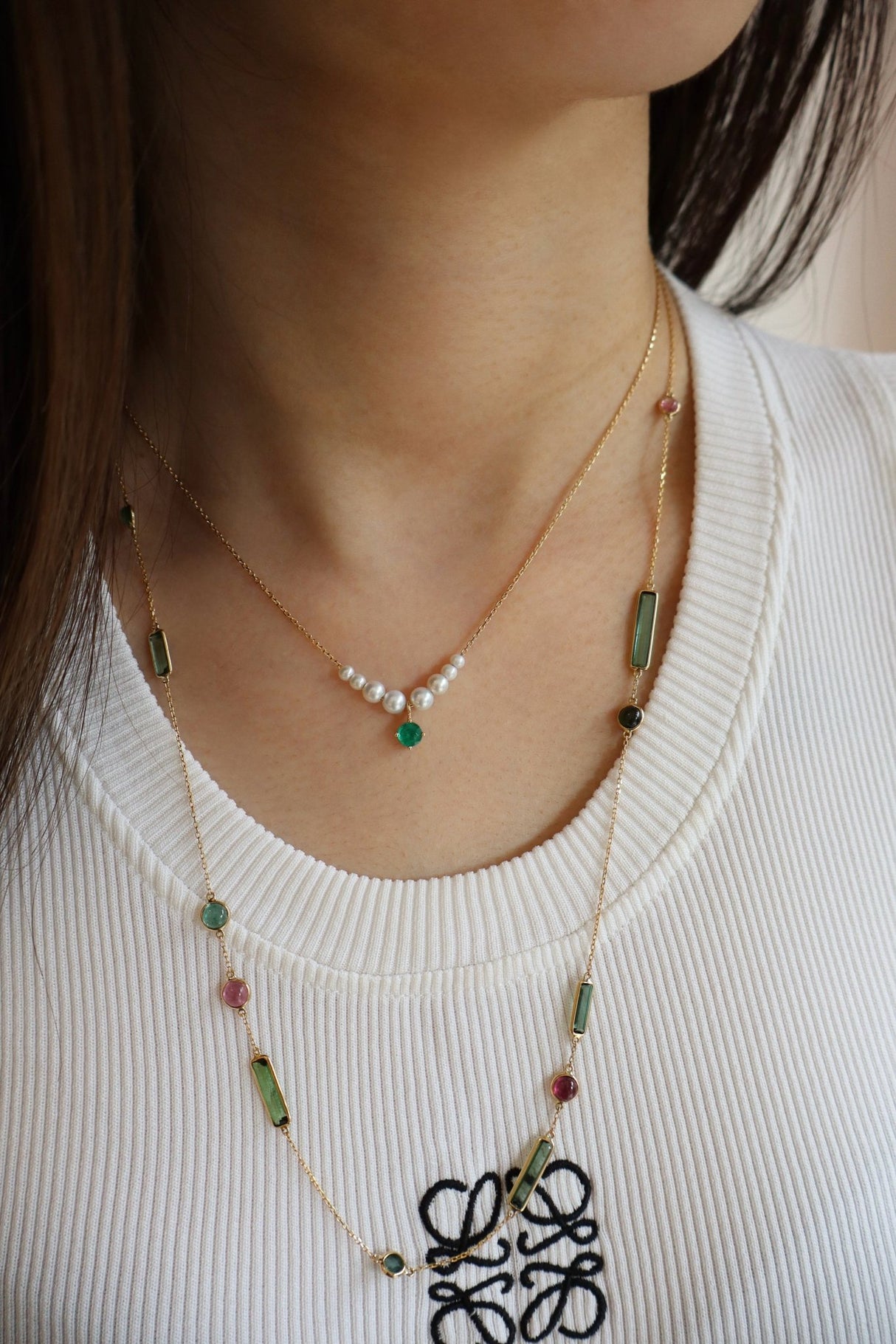 Close-up of a person wearing a delicate necklace with green and red beads on a white background