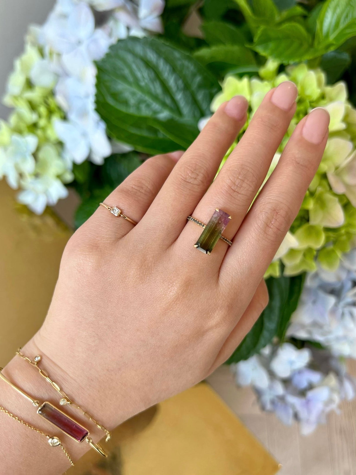 Hand wearing a ring with a green gemstone against a floral background