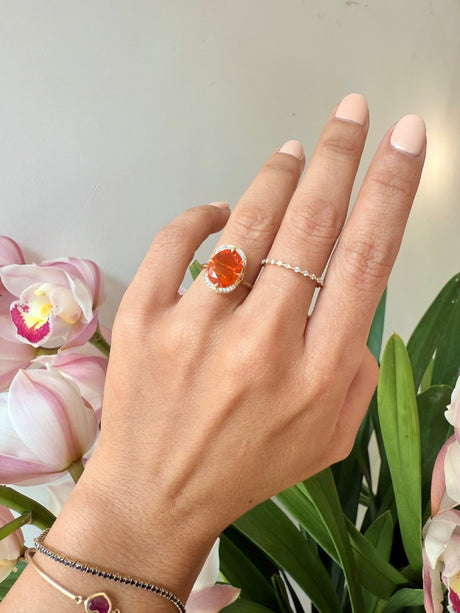 Fire opal engagement ring in 18k gold worn on model against a floral background