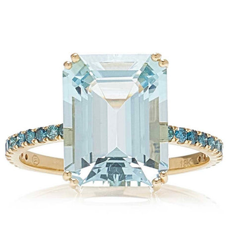 An 18K gold ring with a large emerald-cut aquamarine centerpiece and smaller blue diamond accents along the band.
