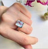 An 18K gold ring with a large emerald-cut aquamarine centerpiece and smaller blue diamond accents along the band. Perfect engagement ring or wedding ring in 18k gold. 