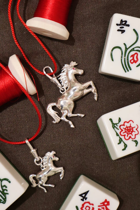 Silver horse pendant on red thread with Mahjong tiles on a brown background