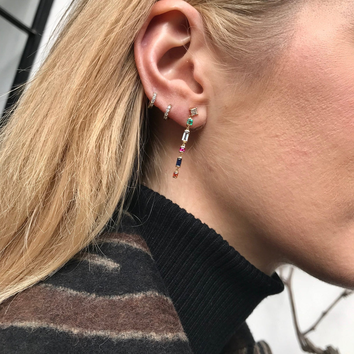 Close-up of an ear wearing colorful drop earrings in 18k gold with a blurred background