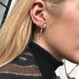 Close-up of an ear wearing colorful drop earrings in 18k gold with a blurred background