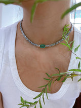 A necklace featuring a series of linked gemstones, with larger emerald cuts at the center and smaller aquamarine cuts on the sides, handmade by female artisans. Ethically sourced gemstones made into colorful wearable art. 