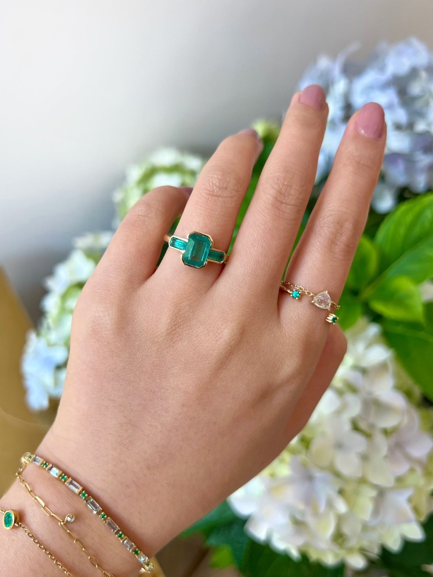 18k gold Emerald Bar Ring worn in a ring stack on model with a floral background