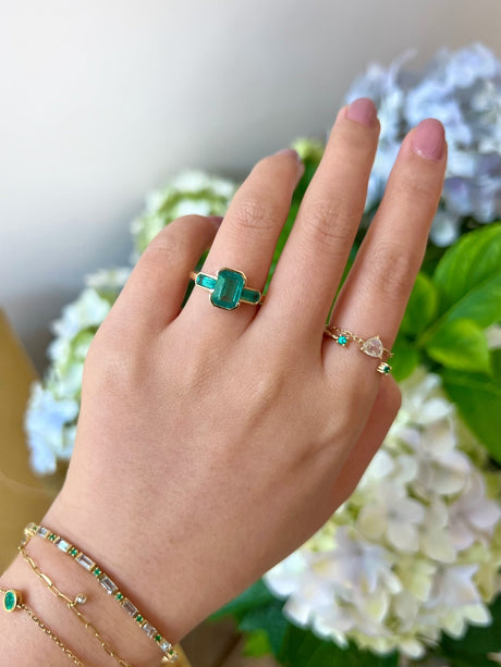 18k gold Emerald Bar Ring worn in a ring stack on model with a floral background