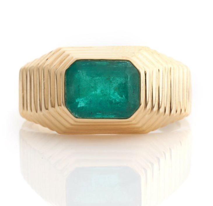 A yellow gold ring with a large emerald set in its center, showcasing a pyramid-like design.