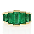 Gold ring with seven emerald green gemstones on a white background