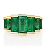 Gold ring with seven emerald green gemstones on a white background