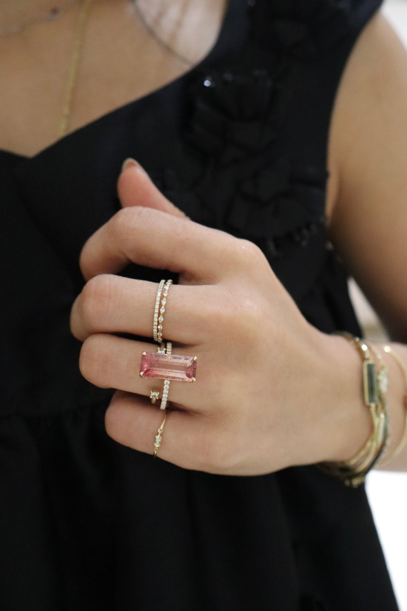 Close-up of a hand wearing a pink gemstone ring with gold band, set against a black background.