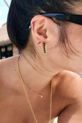 Close-up of an ear with a gold earring and green beads in an earring stack with model wearing sunglasses