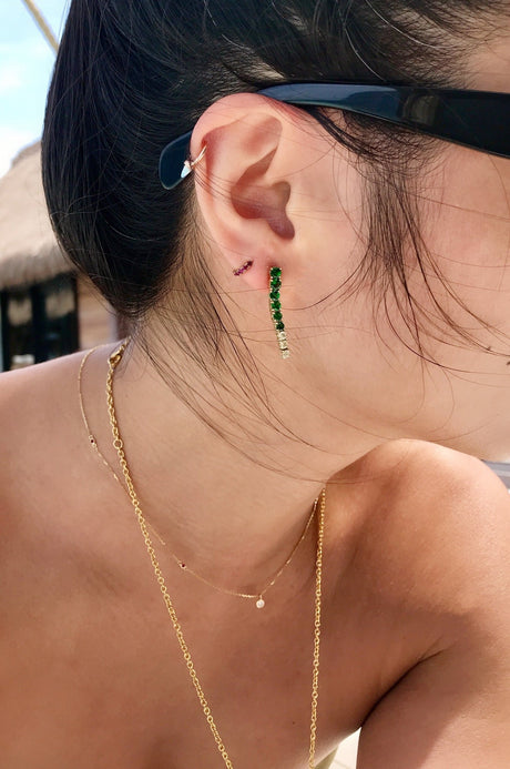 Close-up of an ear with a gold earring and green beads in an earring stack with model wearing sunglasses