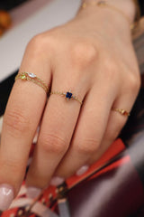 Close-up of a hand wearing a gold ring with a blue gemstone on a blurred background