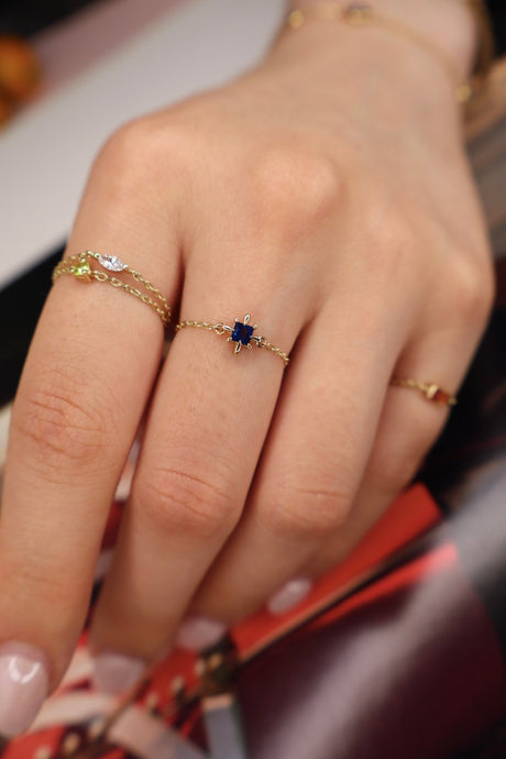 Close-up of a hand wearing a gold ring with a blue gemstone on a blurred background