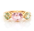 An 18k yellow gold ring with a central pink tourmaline and two mint green tourmaline stones on either side, set against a white background.