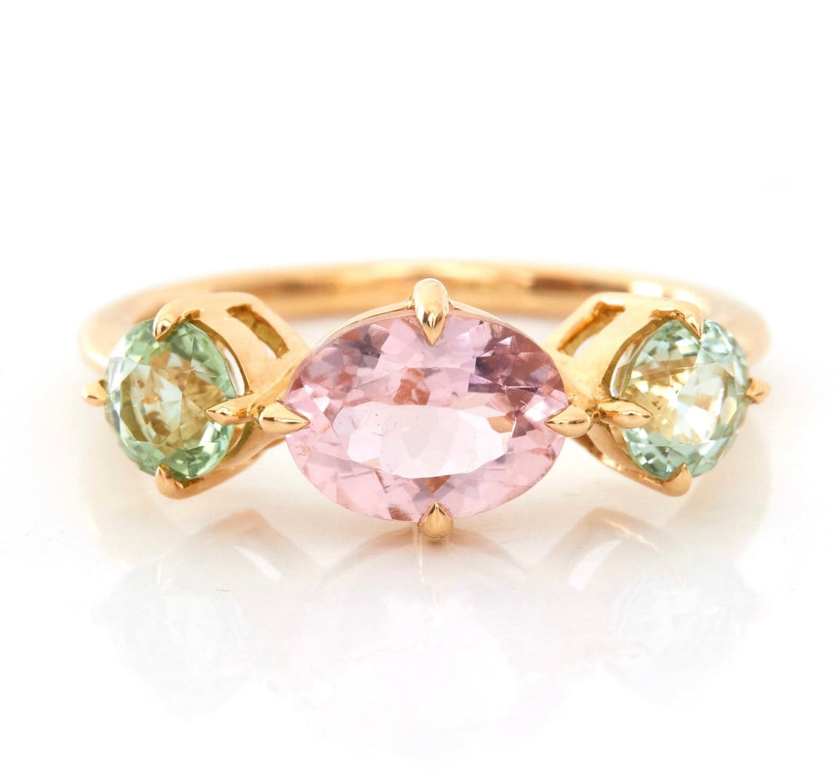 An 18k yellow gold ring with a central pink tourmaline and two mint green tourmaline stones on either side, set against a white background.