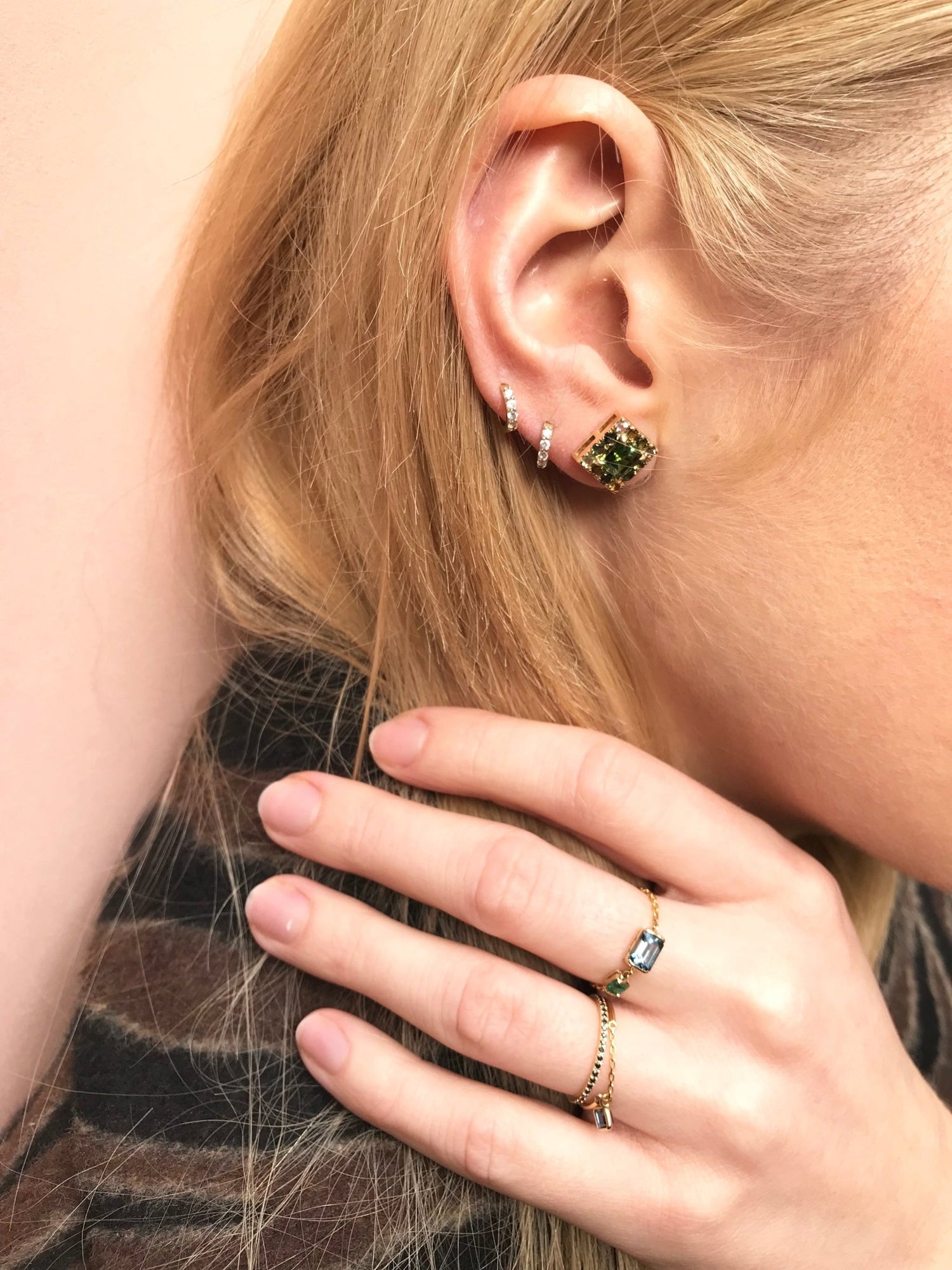 Close-up of a person wearing green gemstone earrings and rings on a neutral background