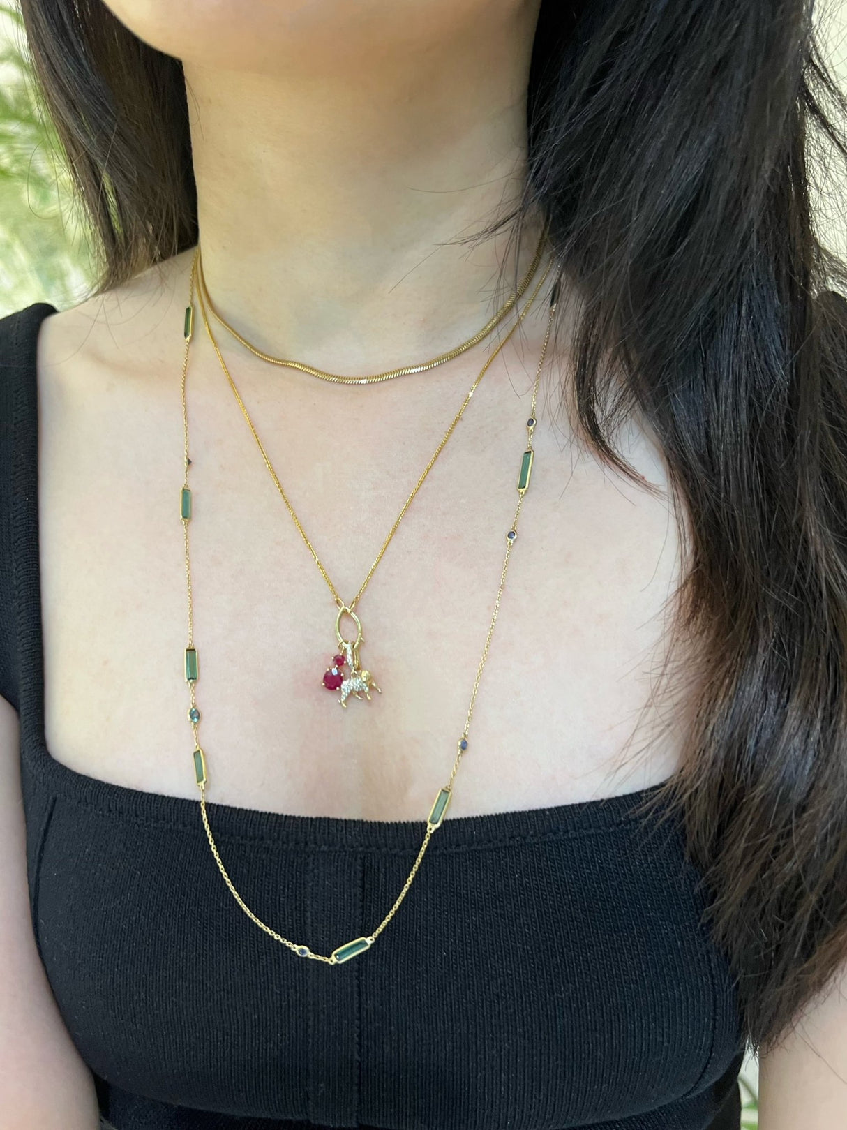 Person wearing a gold necklace with green beads and a small pendant.