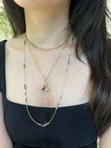 Person wearing a gold necklace with green beads and a small pendant.