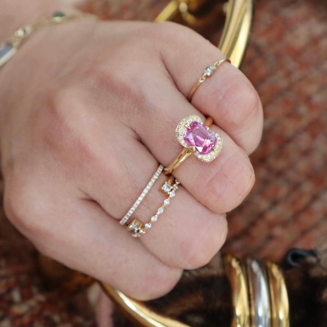 Close-up of a hand wearing a pink gemstone ring with gold band against a blurred background