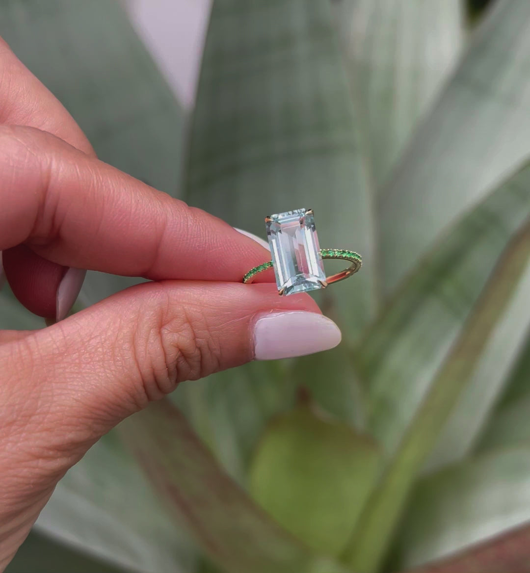 An 18K gold ring with a central aquamarine gem flanked by vivid green emerald gems on the sides. Handmade by female artisans with sustainably mined gemstones. Exquisite and modern in design. 