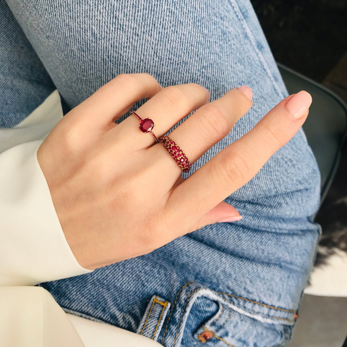 18k yellow gold ring with vivid red and pigeon blood red rubies on a model wearing jeans. Ruby rings stacked on a hand. 