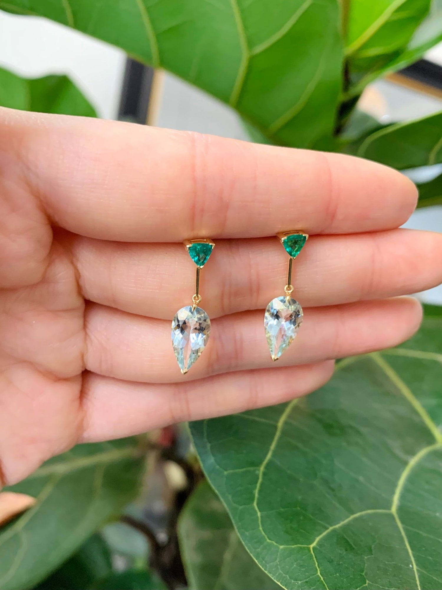 A pair of dangle earrings featuring vivid green tsavorite garnet at the top and clear Aquamarine stones in a teardrop shape at the bottom, set in gold mounting. Handmade by female artisans with sustainably mined gemstones 